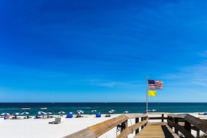 A wooden boardwalk leading to a beach with white sand and a clear blue sky.
