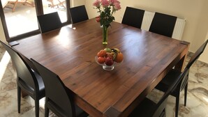 Une table à manger avec des chaises, un vase rempli de fleurs et un saladier de fruits.