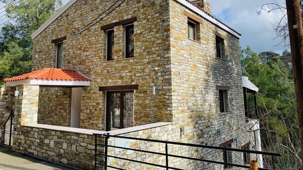 Un bâtiment en pierre avec un toit recouvert de tuiles rouges, un balcon et une entrée fermée par un portail.