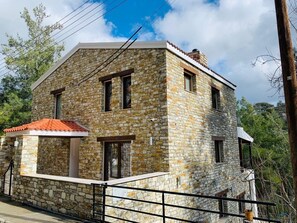 Un bâtiment en pierre avec un toit recouvert de tuiles rouges, un balcon et une entrée fermée par un portail.