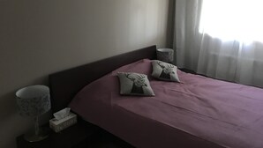 Une chambre d’hôtel avec un lit, des oreillers, une table de chevet, une lampe et une fenêtre avec des rideaux.