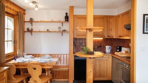 A wooden dining table with chairs, a kitchen with wooden cabinets, a built-in oven, and a window with curtains. - Orchidée 111 by Interhome (Verbier)