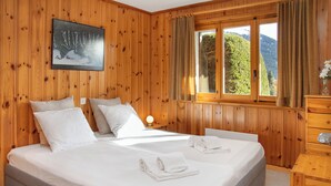 A wooden-paneled bedroom with a large bed, two pillows, a nightstand with a lamp, and a dresser. - Orchidée 111 by Interhome (Verbier)