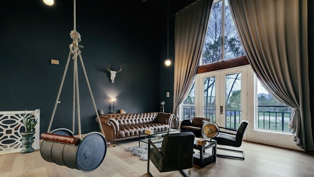 A living room with a hanging barrel chair, a leather sofa, and a piano. - Huge Sunlit Loft w/ Indoor Swing and Skyline Views (Houston)