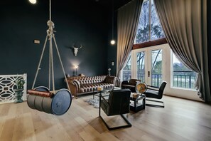 A living room with a hanging barrel chair, a leather sofa, and a piano. - Huge Sunlit Loft w/ Indoor Swing and Skyline Views (Houston)