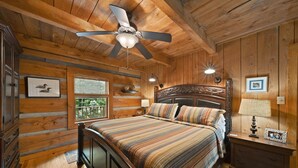 Un dormitorio tipo cabaña de troncos con una cama, techo de madera y ventilador de techo.