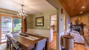 A dining area with a wooden table and chairs, a chandelier, and a view of the outdoors. - Chipmunk View Lodge - Amazing views, hot tub, and manmade waterfall! (Blowing Rock)