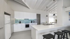 A modern kitchen with white cabinetry, a tiled backsplash, and a central island with bar stools.