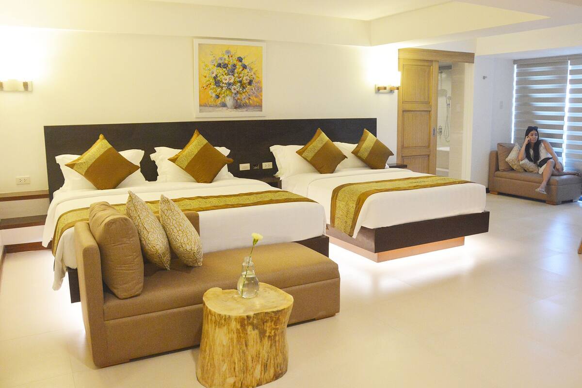 A hotel room with two beds, a wooden side table, and a painting on the wall.