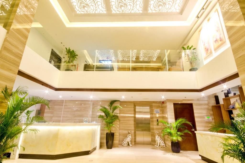 Vestíbulo de hotel con mostrador de recepción, dos ascensores y plantas decorativas en macetas.