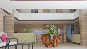 A modern lobby with a reception desk, a seating area with a table and chairs, and a decorative wooden sculpture. - Commander Suites de Boracay (Boracay Island)