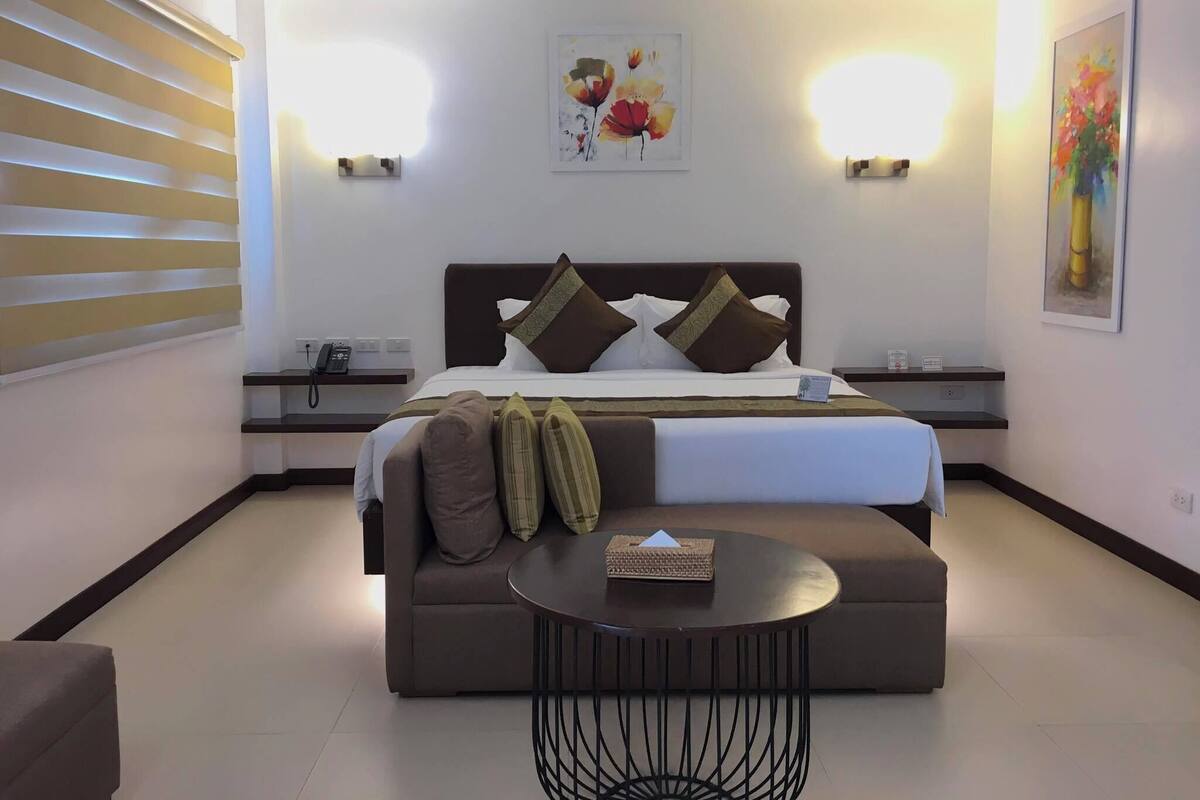 A hotel room with a bed, a sofa, a small round table, and two wall-mounted lights.