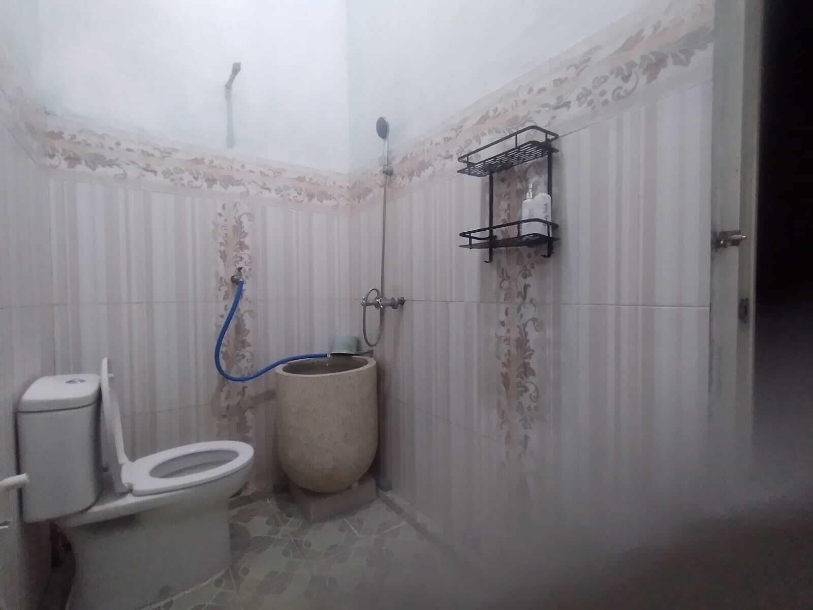 A small bathroom with a toilet, a shower, and a wall-mounted shelf.
