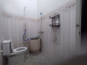 A small bathroom with a toilet, a shower, and a wall-mounted shelf.