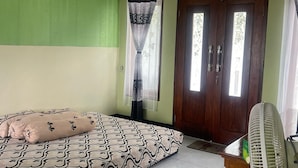 Una habitación con una cama, un ventilador, una puerta con ventanal y un cuadro en la pared.
