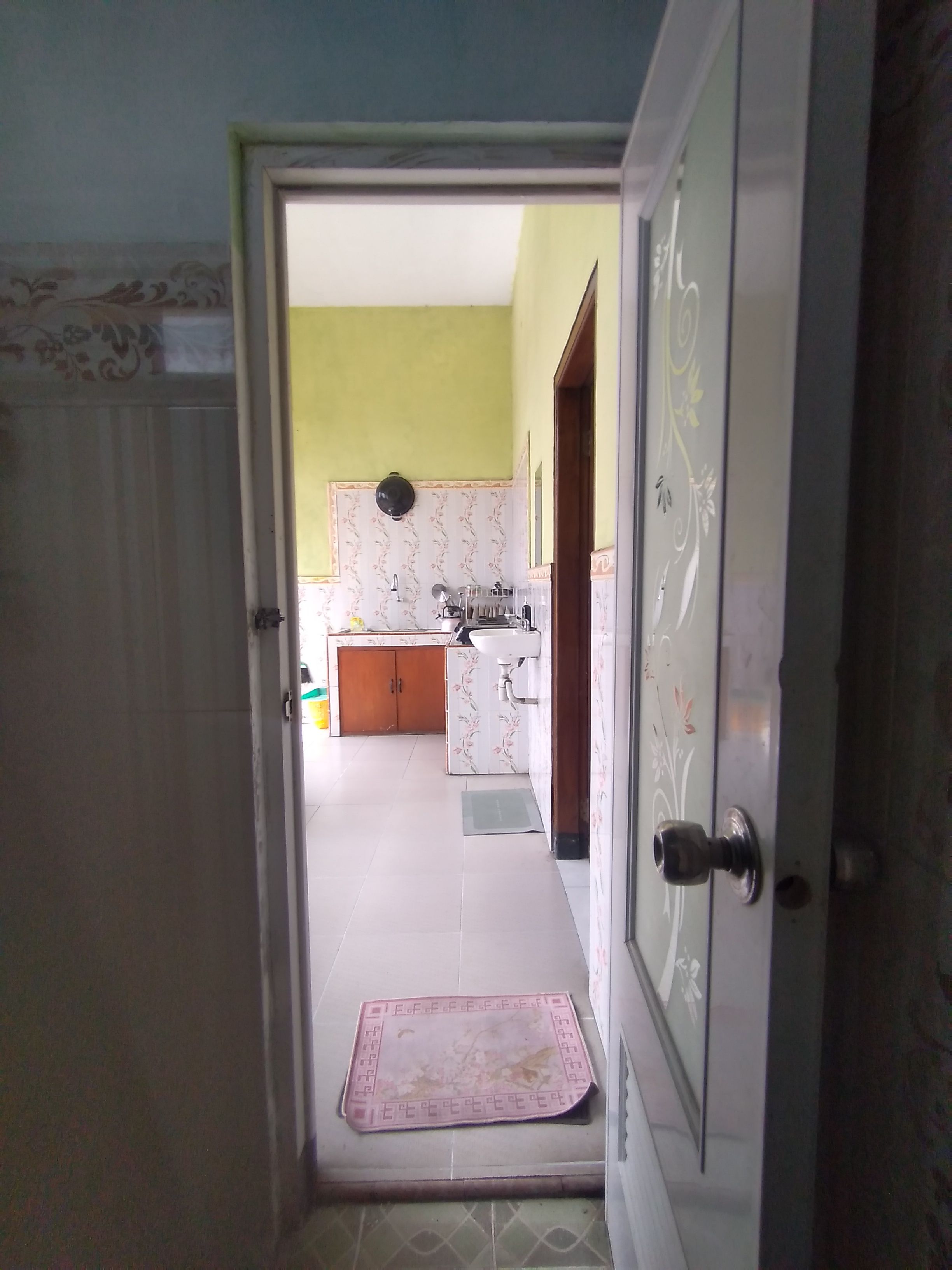 Una puerta abierta que da a una cocina con piso de baldosas, un lavamanos, armarios y un felpudo.