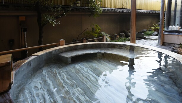 A traditional Japanese onsen with a wooden deck and a stone basin. - Isawa Tokiwa Hotel (Fuefuki)