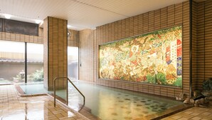 A traditional Japanese onsen with a large mural, tiled walls, and a stone bath area. - Isawa Tokiwa Hotel (Fuefuki)
