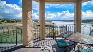 Un balcon avec une table et des chaises, donnant sur une étendue d’eau et un paysage lointain.