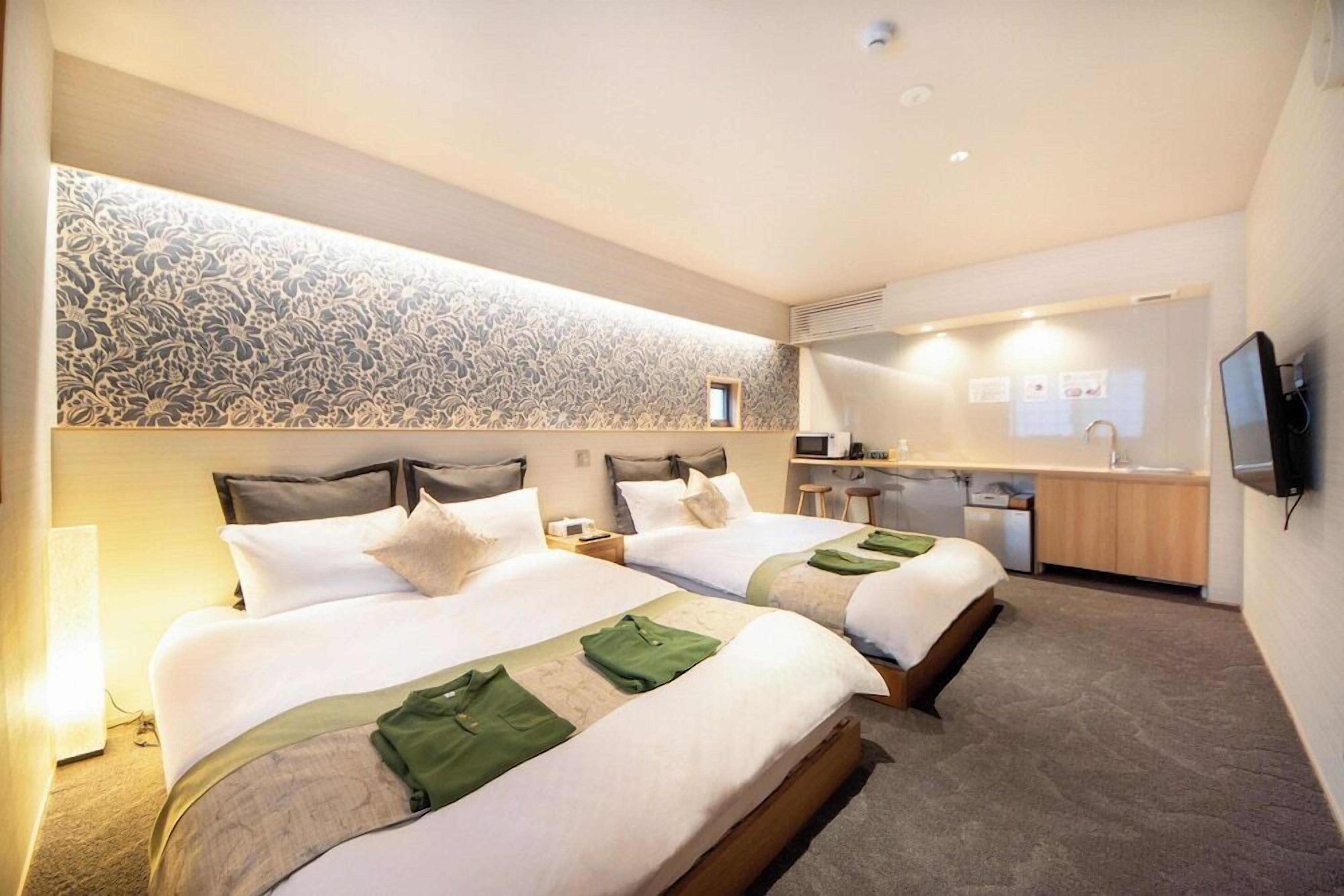 A hotel room with two beds, a desk, a mirror, and a television.
