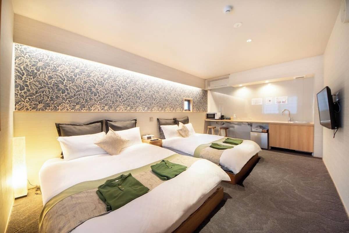 Una habitació d'hotel amb dos llits, un escriptori, un mirall i una televisió.