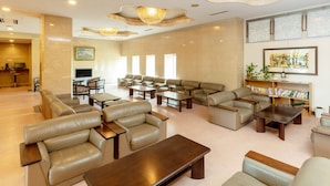 A spacious lobby with leather sofas, wooden coffee tables, and a chandelier. - Tabist Yabuki Station Hotel (Yabuki)