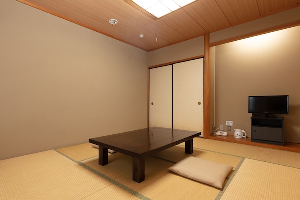 A traditional Japanese room with tatami flooring, a low table, a cushion, a television, and a sliding door.