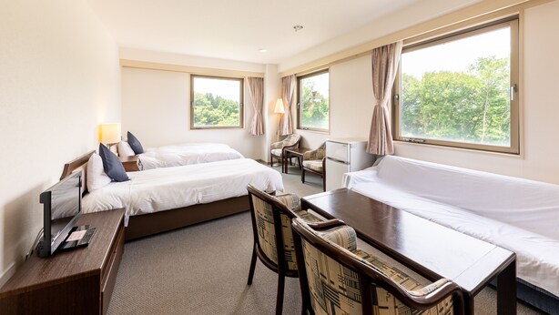 A hotel room with two beds, a desk, a chair, a small table, and large windows with curtains. - Tabist Yabuki Station Hotel (Yabuki)