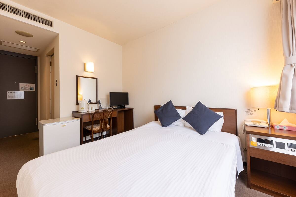 A hotel room with a large bed, a desk with a computer, a chair, a lamp, and a telephone.