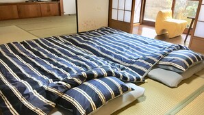 A traditional Japanese-style room with tatami flooring, a futon bed with striped bedding, and a sliding shoji screen door. - Rikyuan Sen (Izumisano)