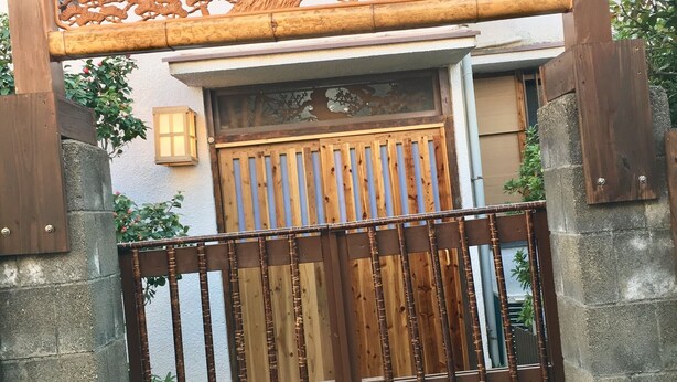 A wooden gate with vertical bars and a decorative overhead structure. - Rikyuan Sen (Izumisano)