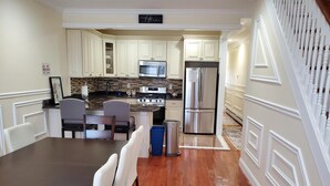 A kitchen with white cabinetry, a stainless steel refrigerator, and a dining area with a table and chairs.