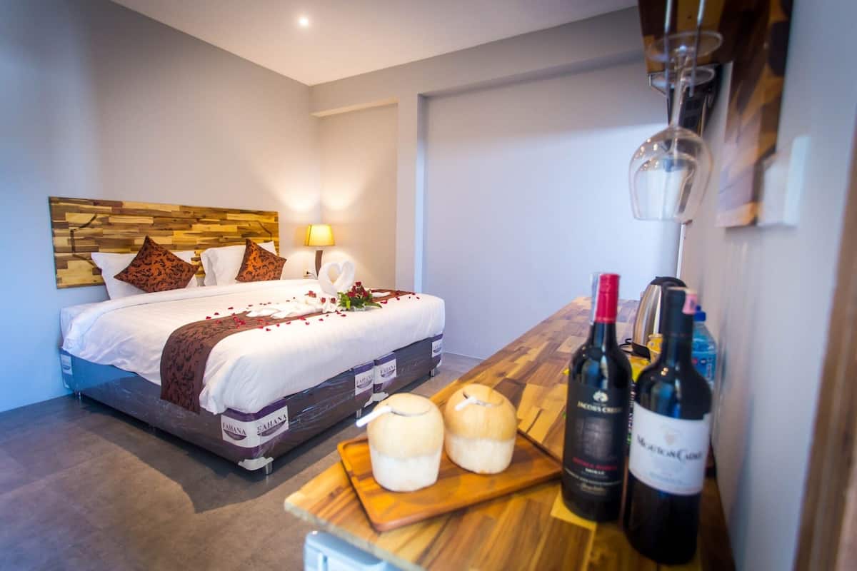 A hotel room with a bed, a wooden headboard, a bedside table with wine bottles, and a small table with candles.