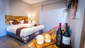 A hotel room with a bed, a wooden headboard, a bedside table with wine bottles, and a small table with candles.