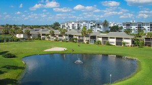 Un campo de golf con un estanque, rodeado de edificios de varios pisos con balcones.