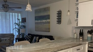 Una cocina moderna con armarios blancos, una isla de mármol y un ventilador de techo.
