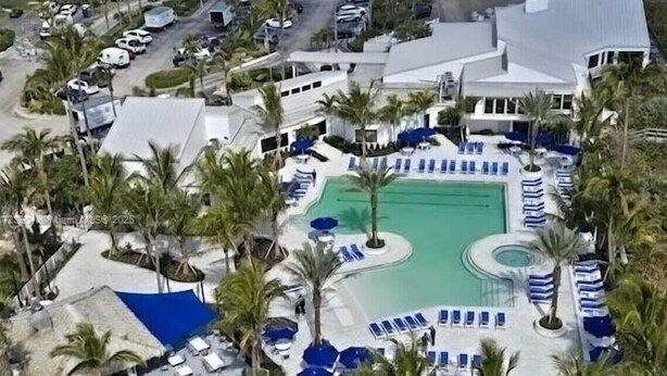 Vista aérea de un complejo turístico con piscina, tumbonas y palmeras.