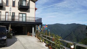 Un edificio de varios pisos con un balcón, estacionamiento y vistas a montañas.
