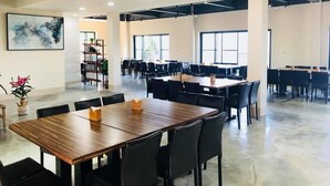 Un espacio interior amplio con varias mesas y sillas, ventanas grandes y un diseño de techo moderno.