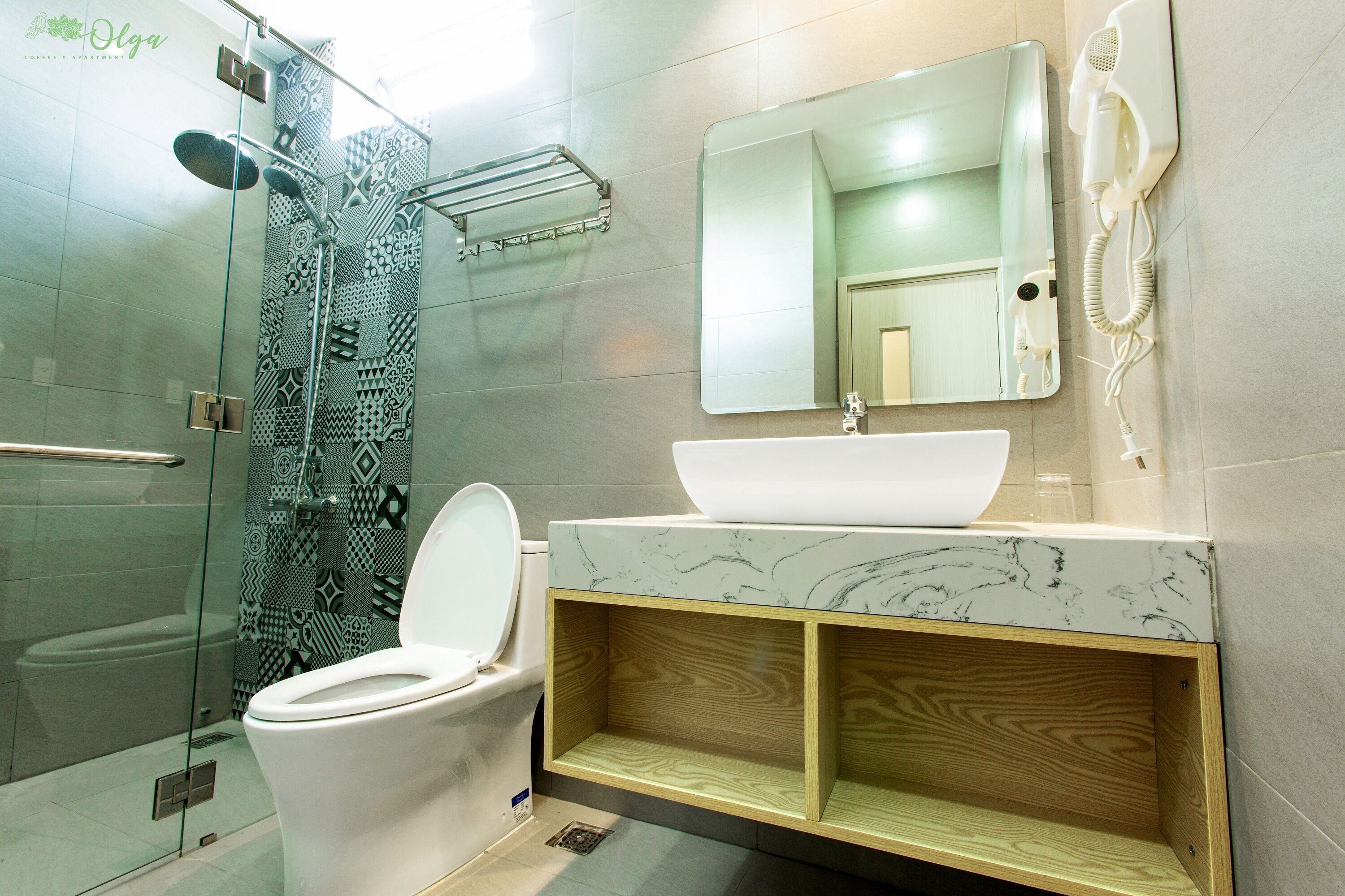 A modern bathroom with a glass shower enclosure, a white toilet, a vanity with a sink and mirror, and a hairdryer mounted on the wall.