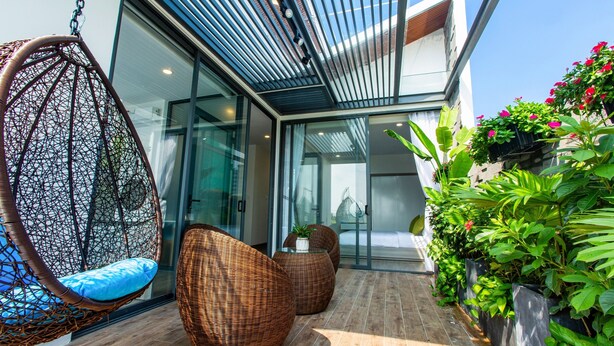 Un espace extérieur moderne aménagé avec des meubles en osier, un fauteuil suspendu et des plantes en pot.