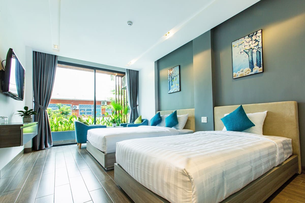 Une chambre d’hôtel avec deux lits, une télévision, un bureau et une vue sur la verdure.
