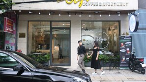 Un immeuble abritant un café et des appartements, doté d’une grande baie vitrée et d’un espace extérieur aménagé pour les clients.