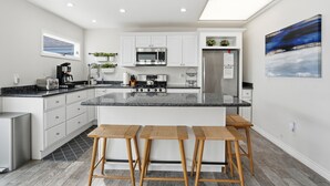 Cocina moderna con armarios blancos, una isla grande, taburetes de bar y un cuadro en la pared.