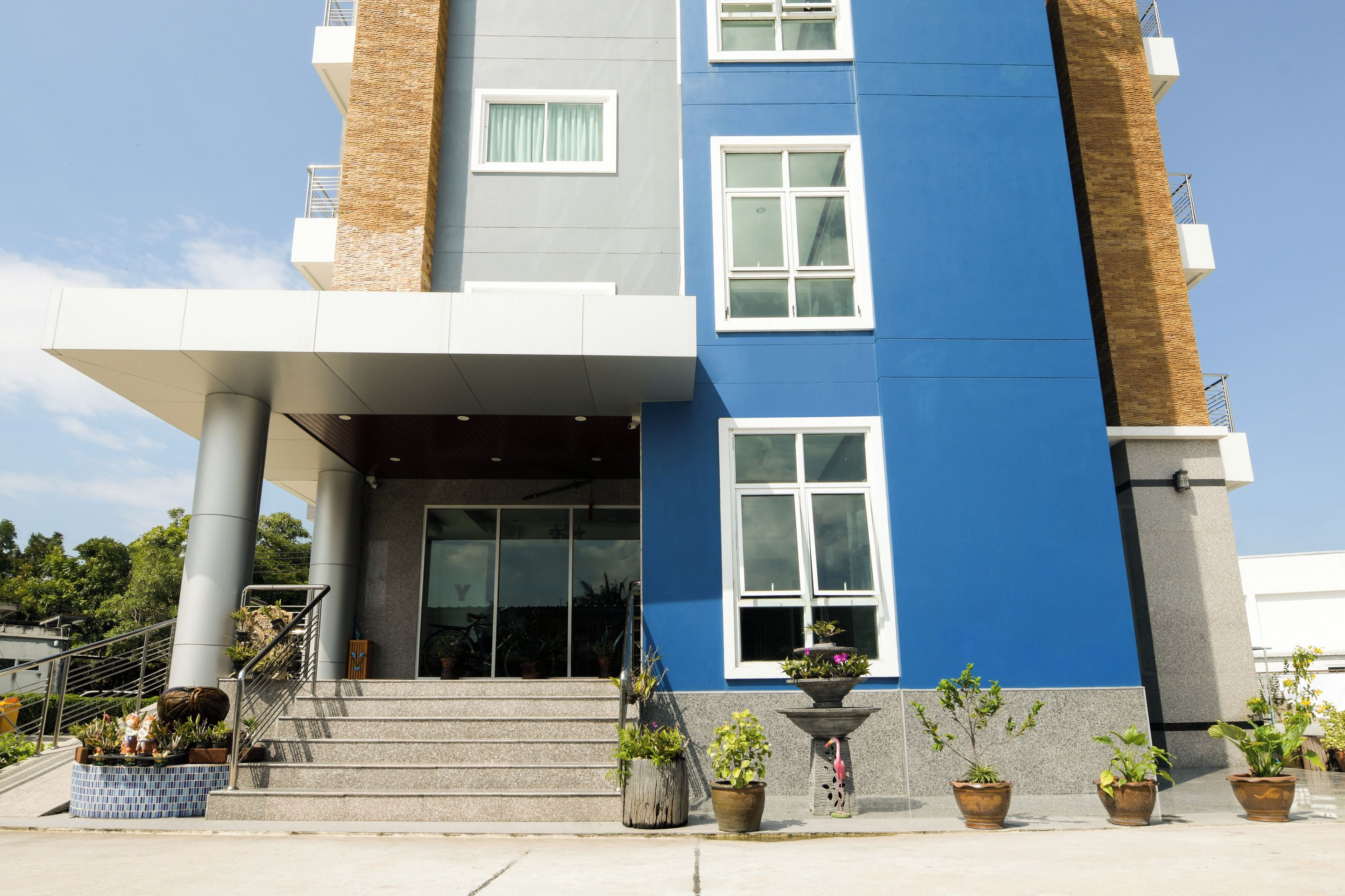 A modern building with a blue and gray facade, large windows, and a covered entrance area with steps leading up to it.