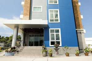 A modern building with a blue and gray facade, large windows, and a covered entrance area with steps leading up to it. - OYO 350 Mae Saeng Place (Si Racha)