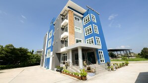 Ein mehrstöckiges Hotel mit blauer und grauer Fassade, einem überdachten Eingangsbereich und einem begrünten Vorbereich mit Pflanzkübeln.