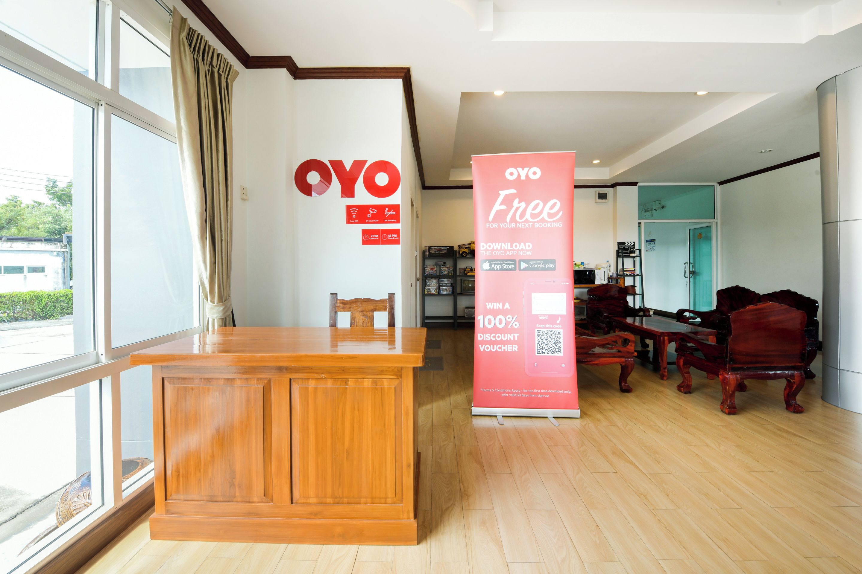 A reception area with a wooden desk, a large OYO sign, and a promotional stand offering a 100% discount voucher.
