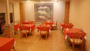 A dining area with tables and chairs, a large mural on the wall, and a brick wall on one side. - Tenshi no Iruka (Ito)