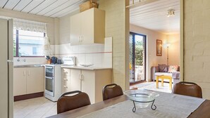 A compact kitchen with a dining area, a built-in oven, and a large window. - Apollo Unit 27 - Ground Floor (Narooma)